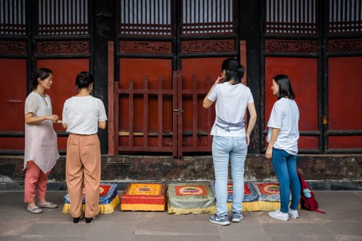 Chengdu, China -  July 2019 :  Four women preparing for a prayer in front of colorful praying kneeling pads in the courtyard of the Buddhist Wenshu Monastery, Sichuan Province