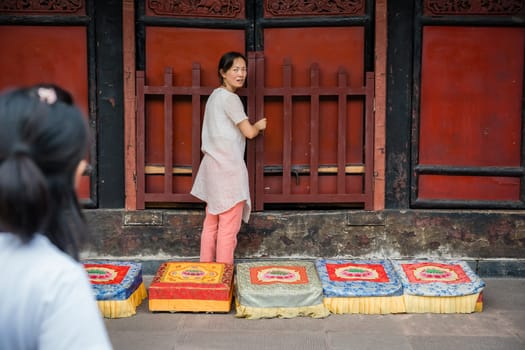 Chengdu, China -  July 2019 :  Chinese woman preparing for a prayer in front of colorful praying kneeling pads in the courtyard of the Buddhist Wenshu Monastery, Sichuan Province