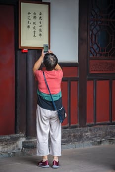 Chengdu, China -  July 2019 :  Chinese woman taking pictures of chinese characters writing displayd on the wall on a temple in the Wenshu Monastery
