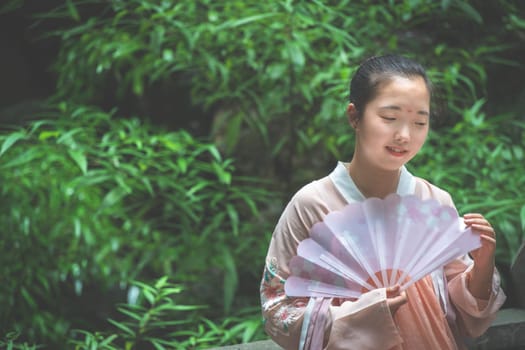 Chengdu, China -  July 2019 :  Portrait of a young asian chinese bride holding a fan at wedding ceremony in the park