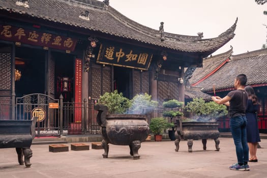 Chengdu, China -  July 2019 : Chinese woman and man praying, worshiping, burning incense sticks, giving alms and thanks at the Wenshu Chinese Buddhist Temple