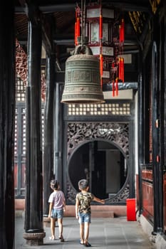Chengdu, China -  July 2019 : Two little boys walking under the large Brass Bell hanging under the roof in Wenshu Monastery