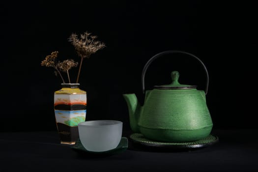 A green metal teapot, a glass bowl and a chinese vase with dried umbels. Isolated on a black background