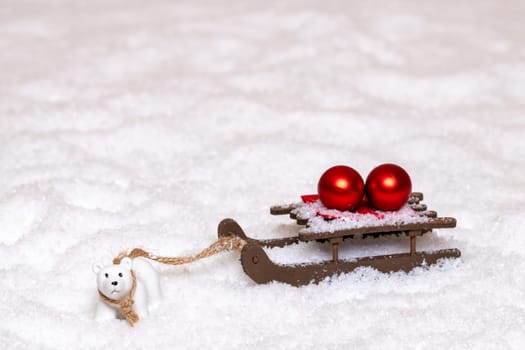 Christmas greeting card template. A little polar bear pulls a sleigh with two red Christmas balls through the snow. Copy space for your design. Macro photograph.