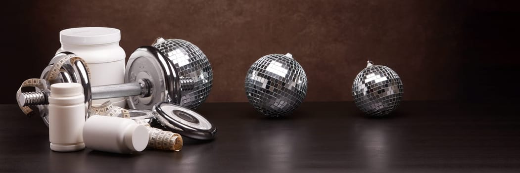 Sports nutrition (supplements), sports equipment and mirror balls on dark brown background with copy space. Fitness, sport or healthy lifestyle concept. New Year and Christmas.