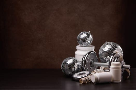 Sports nutrition (supplements), sports equipment and mirror balls on dark brown background with copy space. Fitness, sport or healthy lifestyle concept. New Year and Christmas.