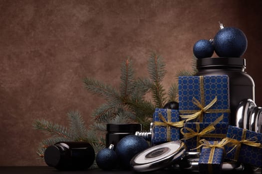 Sports nutrition (supplements), sports equipment, fir branch, gift boxes, Christmas ornaments on dark brown background with copy space. Fitness, sport, healthy lifestyle concept. New Year. Christmas.