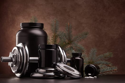 Sports nutrition (supplements), sports equipment and branch of fir, on dark brown background. Fitness, sport or healthy lifestyle concept. New Year and Christmas.