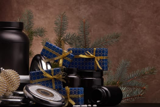 Sports nutrition (supplements), sports equipment, fir branch, gift boxes, Christmas ornaments on dark brown background with copy space. Fitness, sport, healthy lifestyle concept. New Year. Christmas.