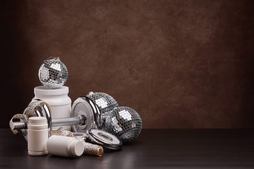 Sports nutrition (supplements), sports equipment and mirror balls on dark brown background with copy space. Fitness, sport or healthy lifestyle concept. New Year and Christmas.