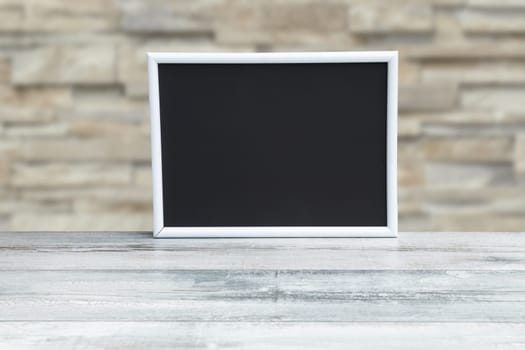 Food recipe template. Empty black board on a rustic wooden table and a blurred stone wall background. For your food product placement or montage. Copy space.