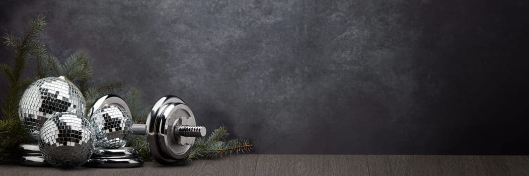 Sports equipment (dumbbell with weights), fir branch, Christmas ornament on dark grey background with copy space. Fitness, sport or healthy lifestyle concept. New Year and Christmas.