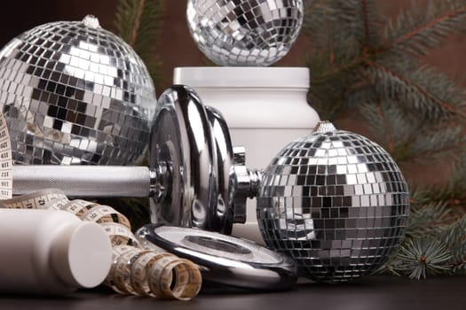 Sports nutrition (supplements), sports equipment, branch of fir, Christmas ornaments on dark brown background. Fitness, sport or healthy lifestyle concept. New Year and Christmas.