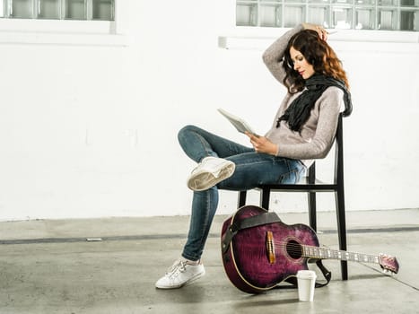 Beautiful redhead sitting on a chair writing songs with acoustic guitar beside her.