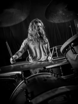 Young long-haired drummer playing his drum set during a concert..