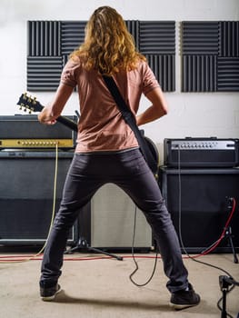 A young man with long hair playing electric guitar in a recording studio..