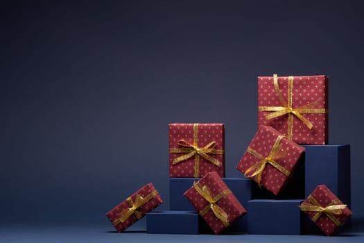 Composition with blue geometric figures and red gift boxes with golden ribbon on dark blue background with copy space. Christmas. New Year. Shopping. Sale. For design of advertising, greeting card