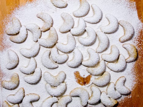 Vanilla crescents covered with powdered sugar on a pastry board with one of them missing