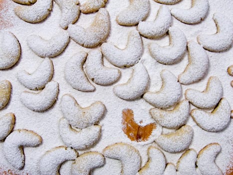 Vanilla crescents covered with powdered sugar on a pastry board with one of them missing