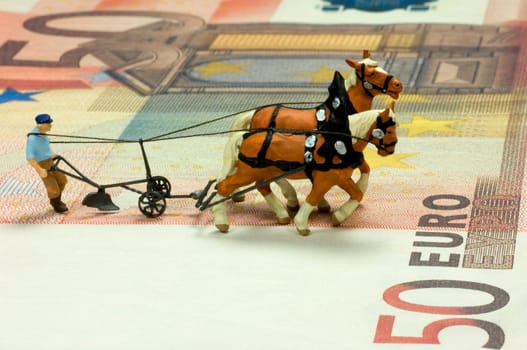 Miniature figure of a ploughman with two horses on a fifty Euro bill. With space for copy.