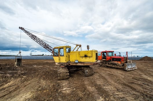 The excavator and old red tractor in the field