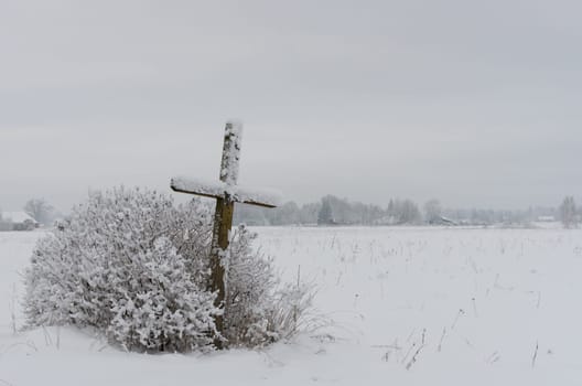 Old weathered wooden catholic cross on a snowy meadow