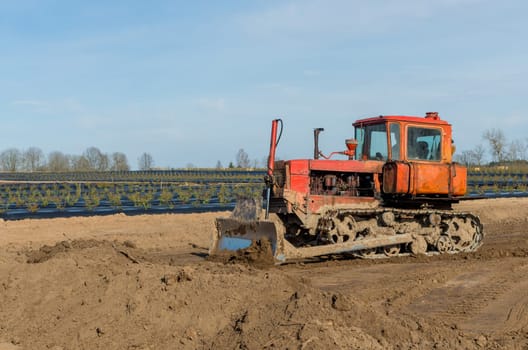 Crawler tractor with a plow on the background of rural landscape