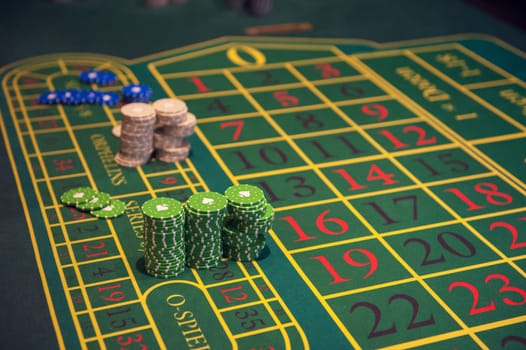 Casino, gambling and entertainment concept - green roulette table with colored chips ready to play