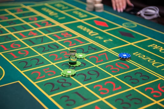 Casino, gambling and entertainment concept - green roulette table with colored chips ready to play