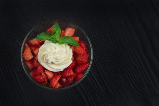 Strawberry with cream decorated with mint leaf on black wooden background