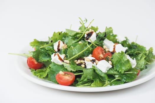 Green salad with vegetables: greens, arugula, tomato, cheese pine nuts and sauce