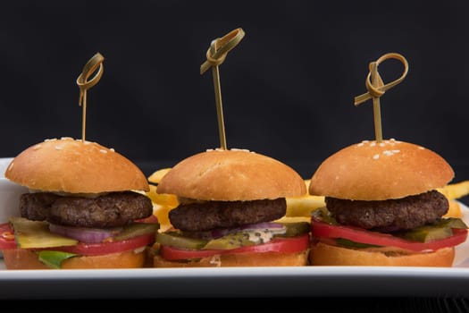 Three mini hamburgers, mini burgers closeup on plate on dark background