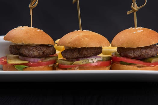 Three mini hamburgers, mini burgers closeup on plate on dark background
