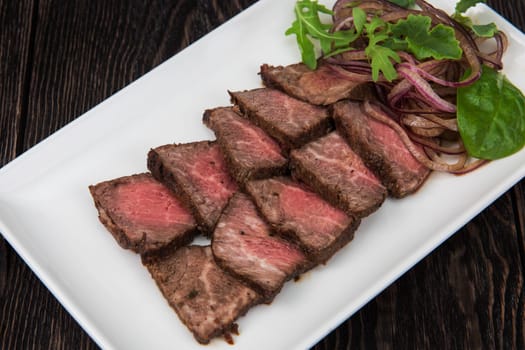 Plate with meat cutting and fresh greens on white plate