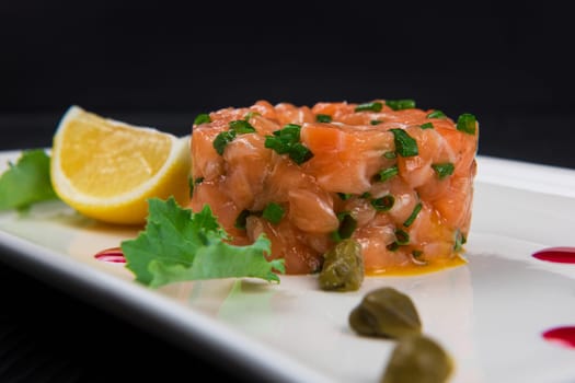Fresh salmon tartare with lime and capers on white plate