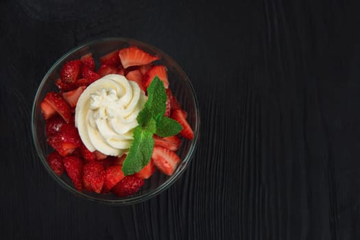 Strawberry with cream decorated with mint leaf on black wooden background