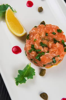 Fresh salmon tartare with lime and capers on white plate