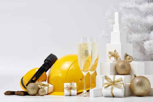 Construction protective earphones and hard hat, fir tree, flutes with champagne, gift boxes and Christmas ornament on a white background. New Year and Christmas construction
