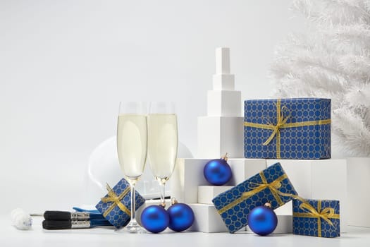 Construction hard hat, white fir tree, two glasses with champagne, gift boxes and Christmas ornaments on a white background. New Year and Christmas construction background