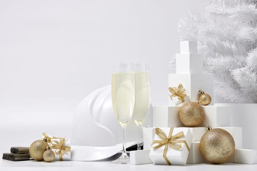 Construction hard hat, white fir tree, two glasses with champagne, gift boxes and Christmas ornaments on a white background. New Year and Christmas construction background