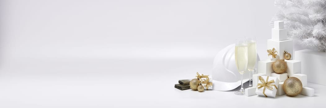 Construction hard hat, white fir tree, two glasses with champagne, gift boxes and Christmas ornaments on a white background with copy space. New Year and Christmas construction background