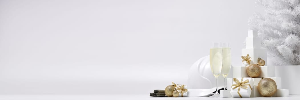 Construction hard hat, white fir tree, two glasses with champagne, gift boxes and Christmas ornaments on a white background with copy space. New Year and Christmas construction background