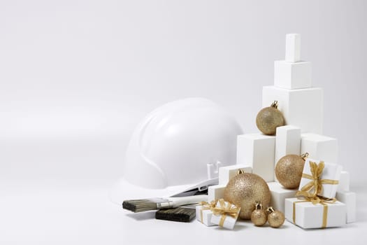 Construction hard hat, white fir tree, gift boxes and Christmas ornament on a white background with copy space. New Year and Christmas construction background