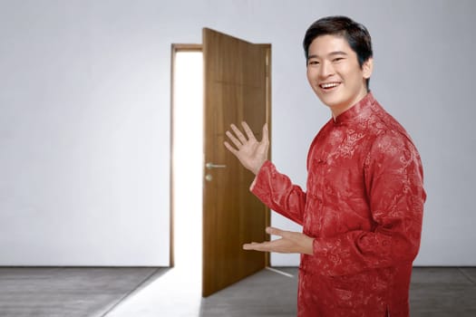 An Asian Chinese man in cheongsam dress invites into the house to celebrate Chinese New Year. Happy Chinese New Year