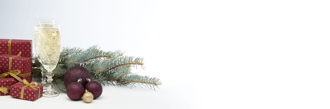 Still life with two champagne flutes, gift boxes and Christmas decoration with fir tree branch on white background with copy space. Christmas and New Year shopping. Greeting card
