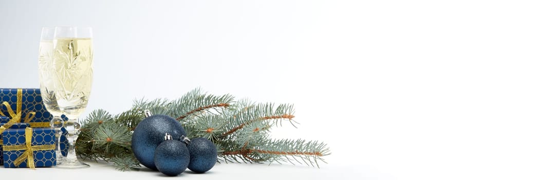 Still life with two champagne flutes, gift boxes and Christmas decoration with fir tree branch on white background with copy space. Christmas and New Year shopping. Greeting card