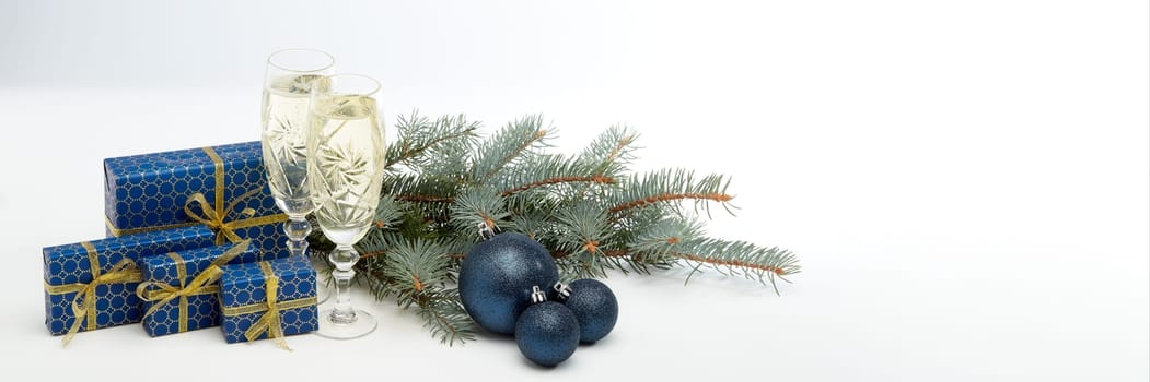 Still life with two champagne flutes, gift boxes and Christmas decoration with fir tree branch on white background with copy space. Christmas and New Year shopping. Greeting card