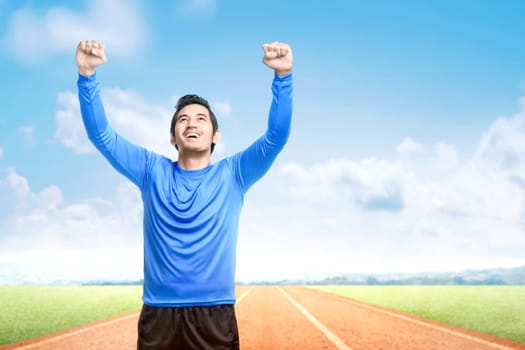 Asian runner man with excited expression after a run on the running track with a blue sky background