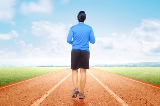 Rear view of Asian runner man running on the running track with a blue sky background