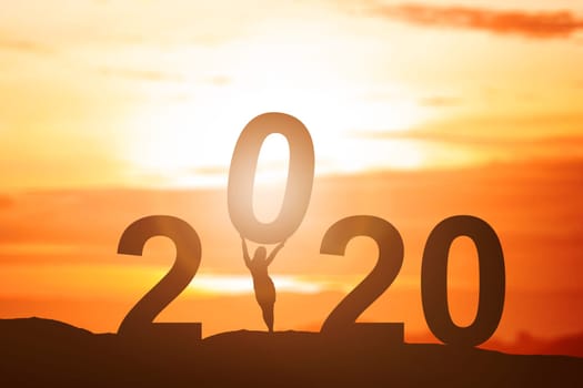 Silhouette of businesswoman put 2020 on the top of the hill with a sunset sky background. Happy New Year 2020